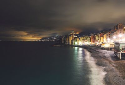 Illuminated buildings by sea against sky at night