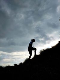 Low angle side view of silhouette man standing on mountain against sky at sunset