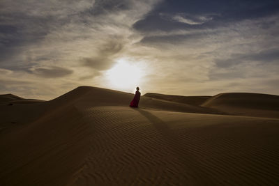 Woman standing on sand dune at desert against sky