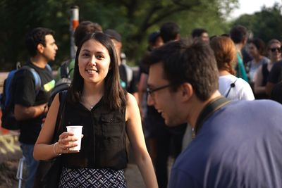 Portrait of young woman holding drink glass during social gathering with friends in background