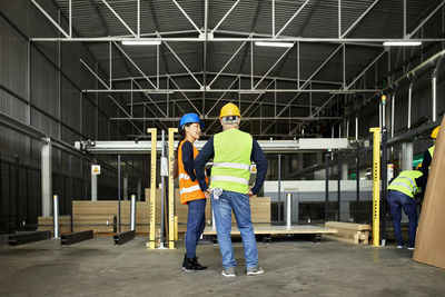 Rear view of male and female worker standing in factory workshop
