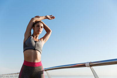 Low angle view of woman exercising against clear blue sky