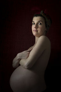 Portrait of young woman standing against black background