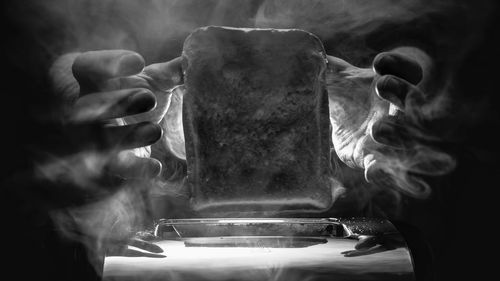 Cropped hands with bread over toaster in darkroom