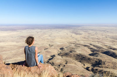 Rear view of woman sitting on rock at desert