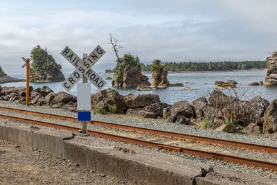Road sign by railroad tracks against sky