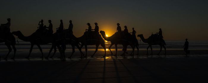 Silhouette people at beach against sky during sunset