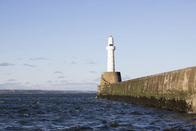 Lighthouse by sea against clear sky