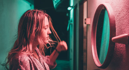 Young woman looking in mirror on wall of building at night