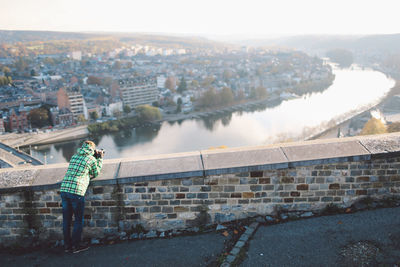 Rear view of woman photographing river amidst buildings in city