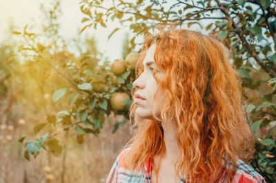 Close-up of thoughtful woman with redhead against fruit tree