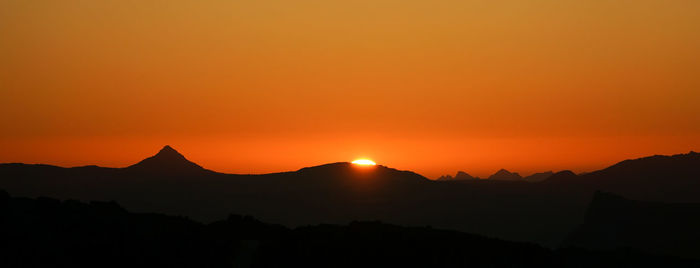 Scenic view of silhouette mountains against orange sky