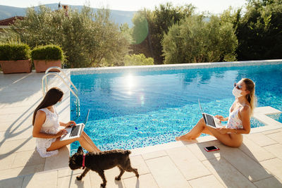 Women sitting by swimming pool against trees