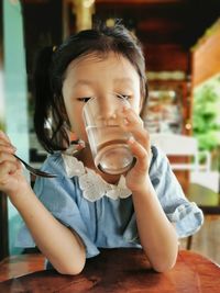 Midsection of girl drinking water from glass on table