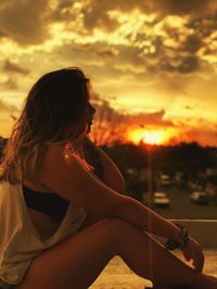 Profile view of woman sitting against cloudy sky during sunset