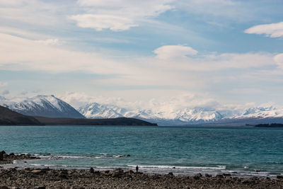 Scenic view of sea by snowcapped mountains against sky