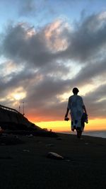 Rear view of silhouette man on car against sky during sunset