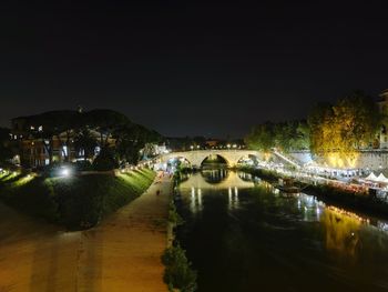 Illuminated buildings by river against sky at night