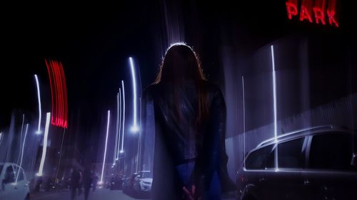 Rear view of woman standing against illuminated lights at night