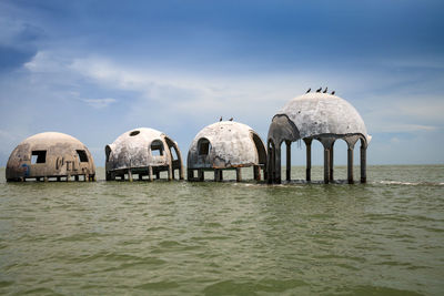 Panoramic view of wooden posts in sea against sky