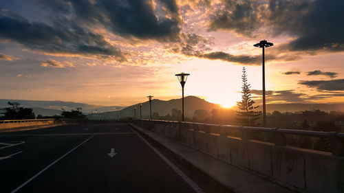 Road by silhouette trees against dramatic sky during sunset