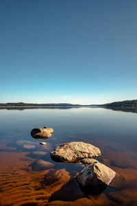Rocks by sea against clear blue sky