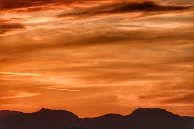 Low angle view of silhouette mountains against orange sky