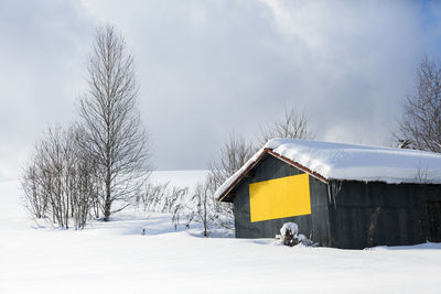 Snow covered house on field against sky during winter