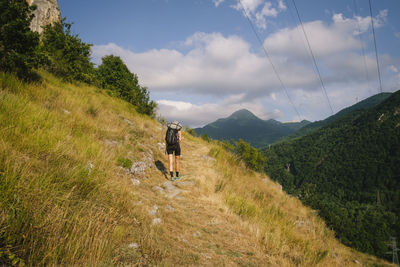 Rear view of man walking on mountain against sky