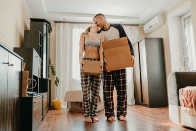 Full length of couple holding boxes kissing while standing at home