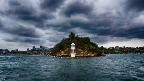 Lighthouse on building by sea against cloudy sky
