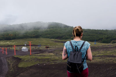 Rear view of woman with backpack standing at field against sky