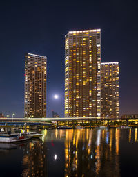 River by illuminated modern buildings against sky at night