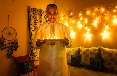 Young man in traditional dress holding the plat fill with oil lamps with ferry lights background