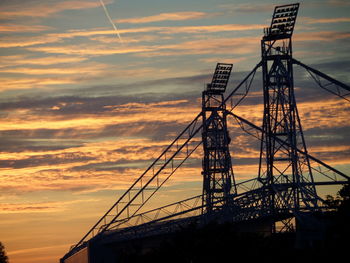 Low angle view of silhouette metallic structures against cloudy sky at sunset