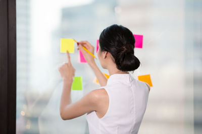 Rear view of a woman writing on sticky paper 