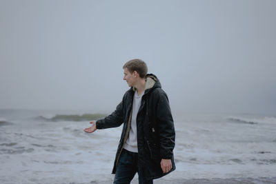 Teenager for the first time at sea, with a smile on his face, shows with his hand what big waves