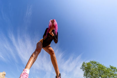 Low angle view of young woman jumping against sky