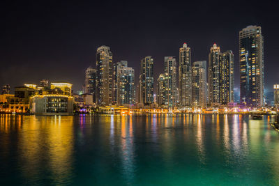 Illuminated buildings by river against sky at night