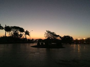 Silhouette trees by lake against clear sky during sunset