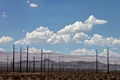 Electricity pylons in desert against cloudy sky