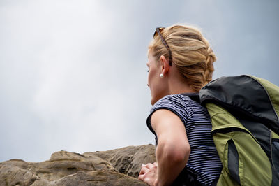 Low angle view of young woman leaning on rock against sky