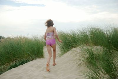 Rear view of teenage girl running amidst bushes at sandy beach
