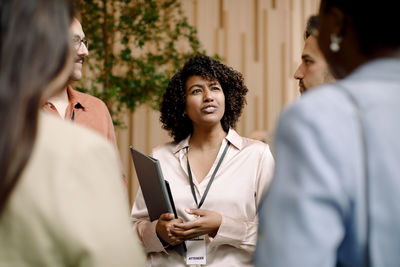 Businesswoman holding folder and discussing with male and female delegates in seminar at convention center