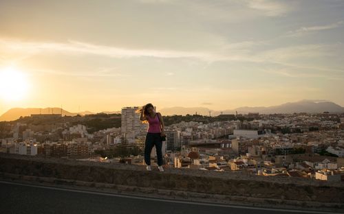 Woman standing against cityscape during sunset