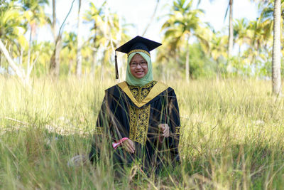 Portrait of smiling young woman wearing graduation gown while standing on field