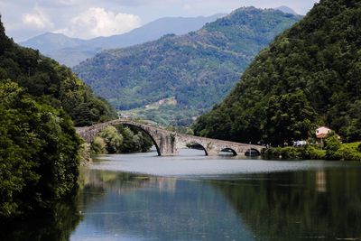 Arch bridge over river by mountains against sky