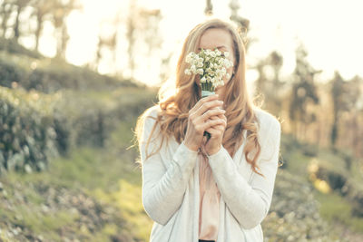 Close-up female hands holding a bouquet of snowdrops in front of their face