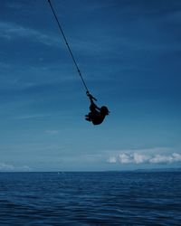 Low angle view of man hanging on rope in sea against sky