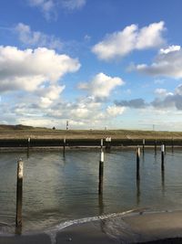 Wooden posts in lake against sky